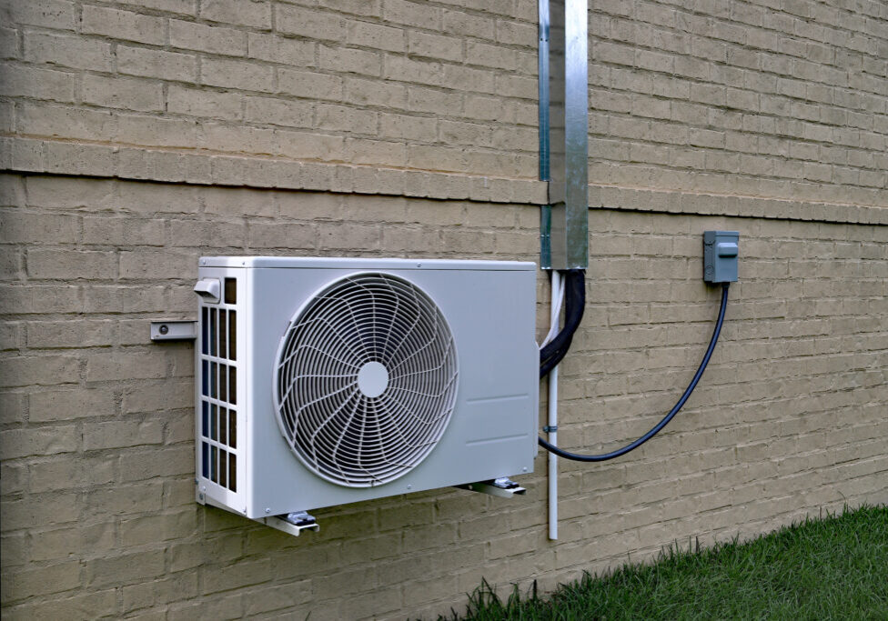 Air Conditioner mini split system next to home with painted brick wall and space for text copy